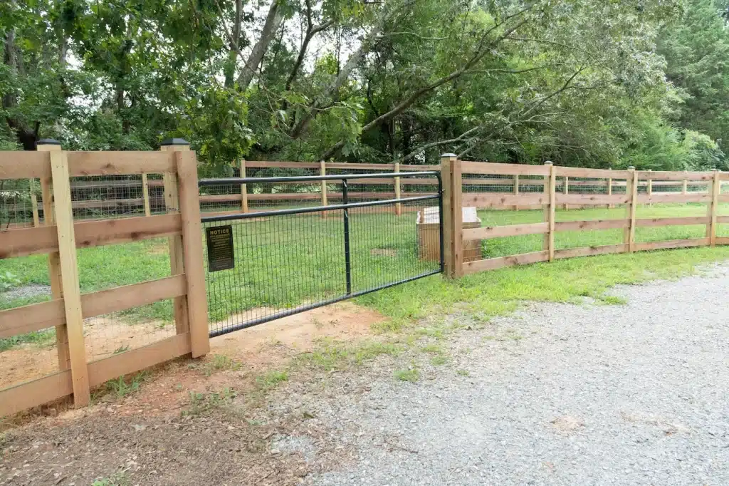 4 board wood paddock fence with a black wire gate along a gravel drive in Goochland