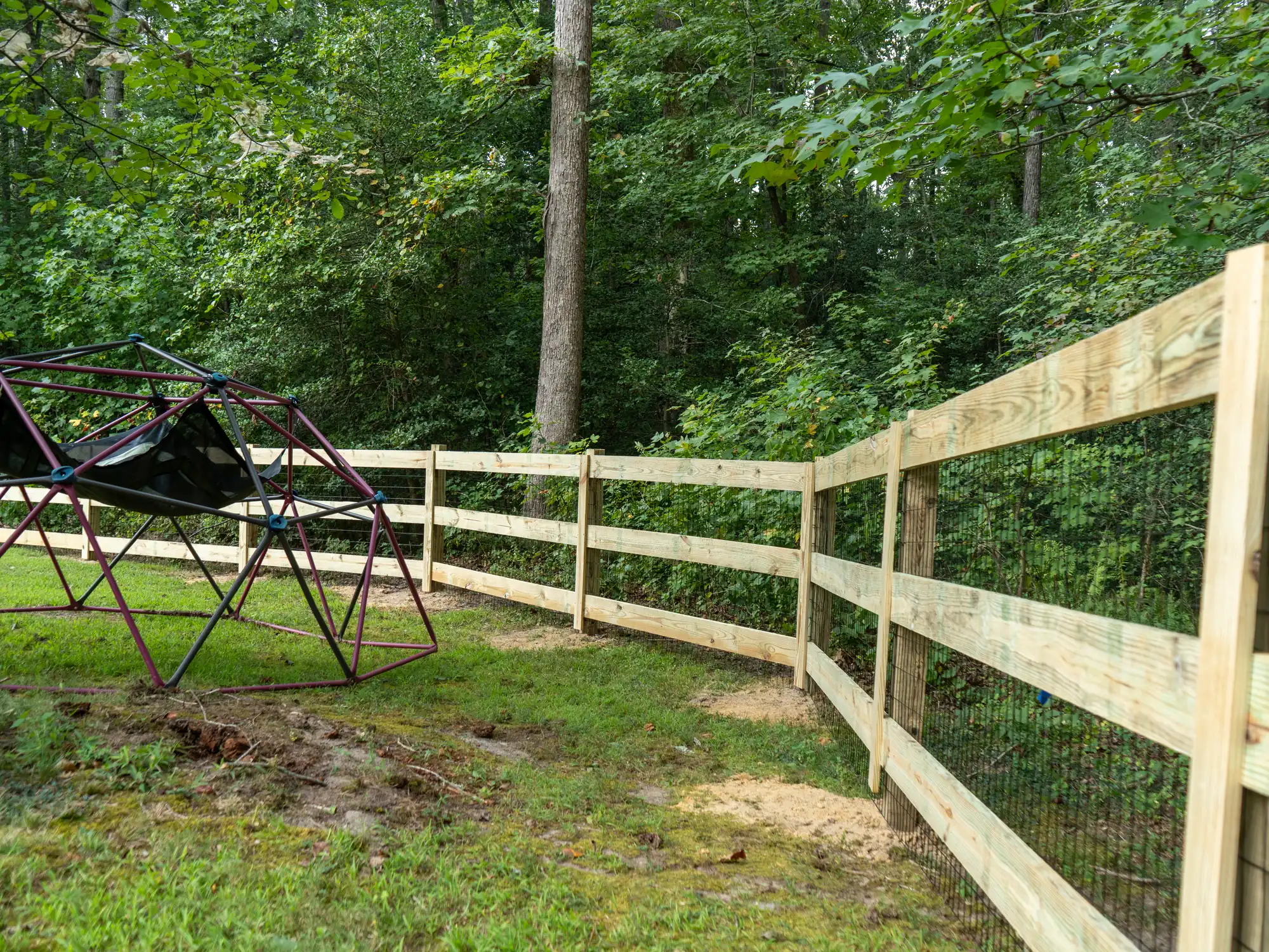 Pressure-treated paddock fence with wire backing wrapping around a play area