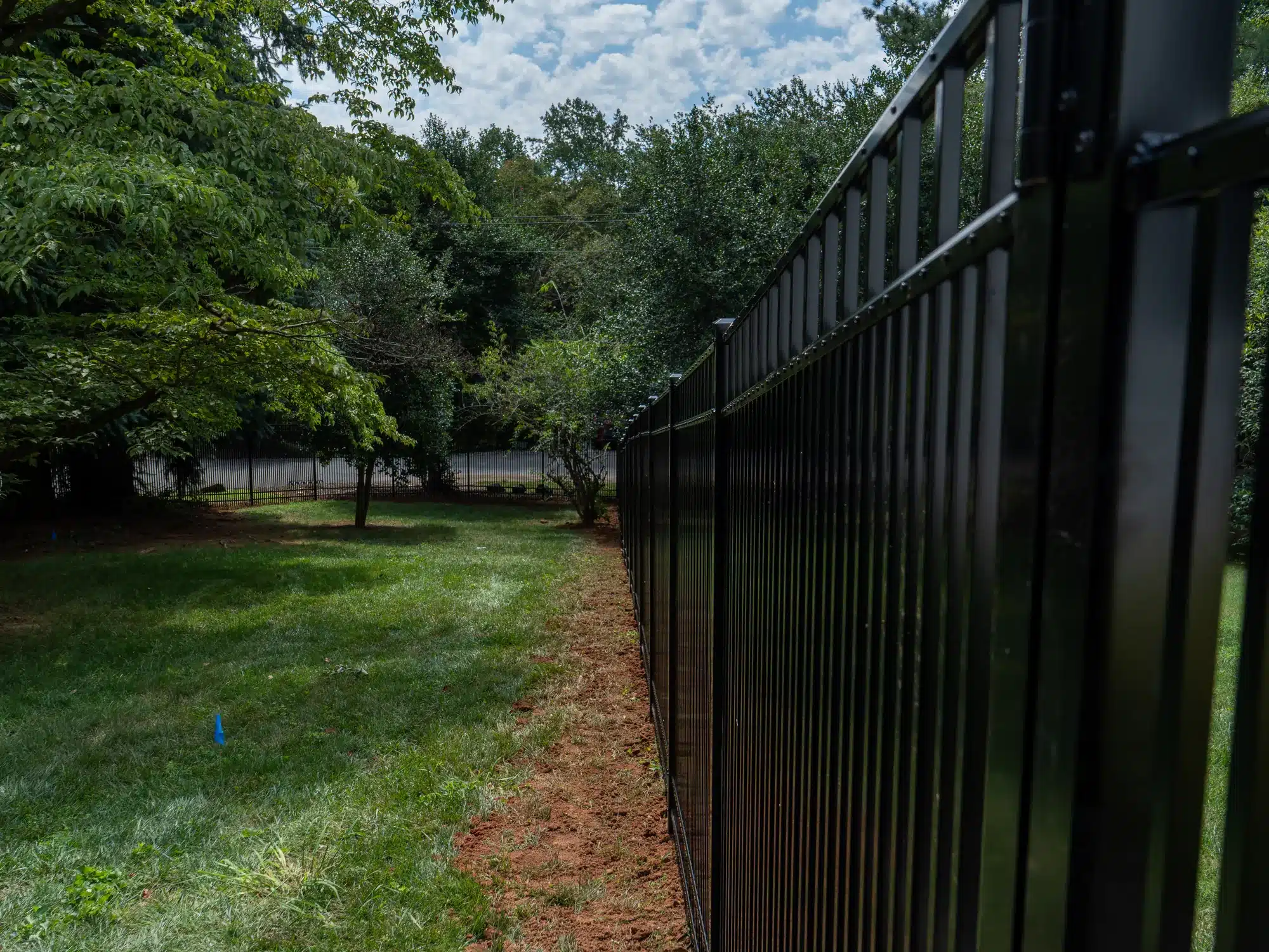 Row of black aluminum fence pickets running along a lawn under mature trees