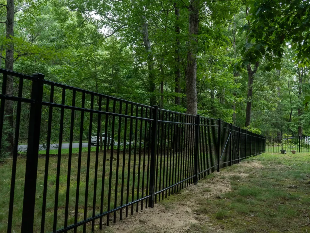 Racked black aluminum fence panels following a wooded slope in Henrico, VA