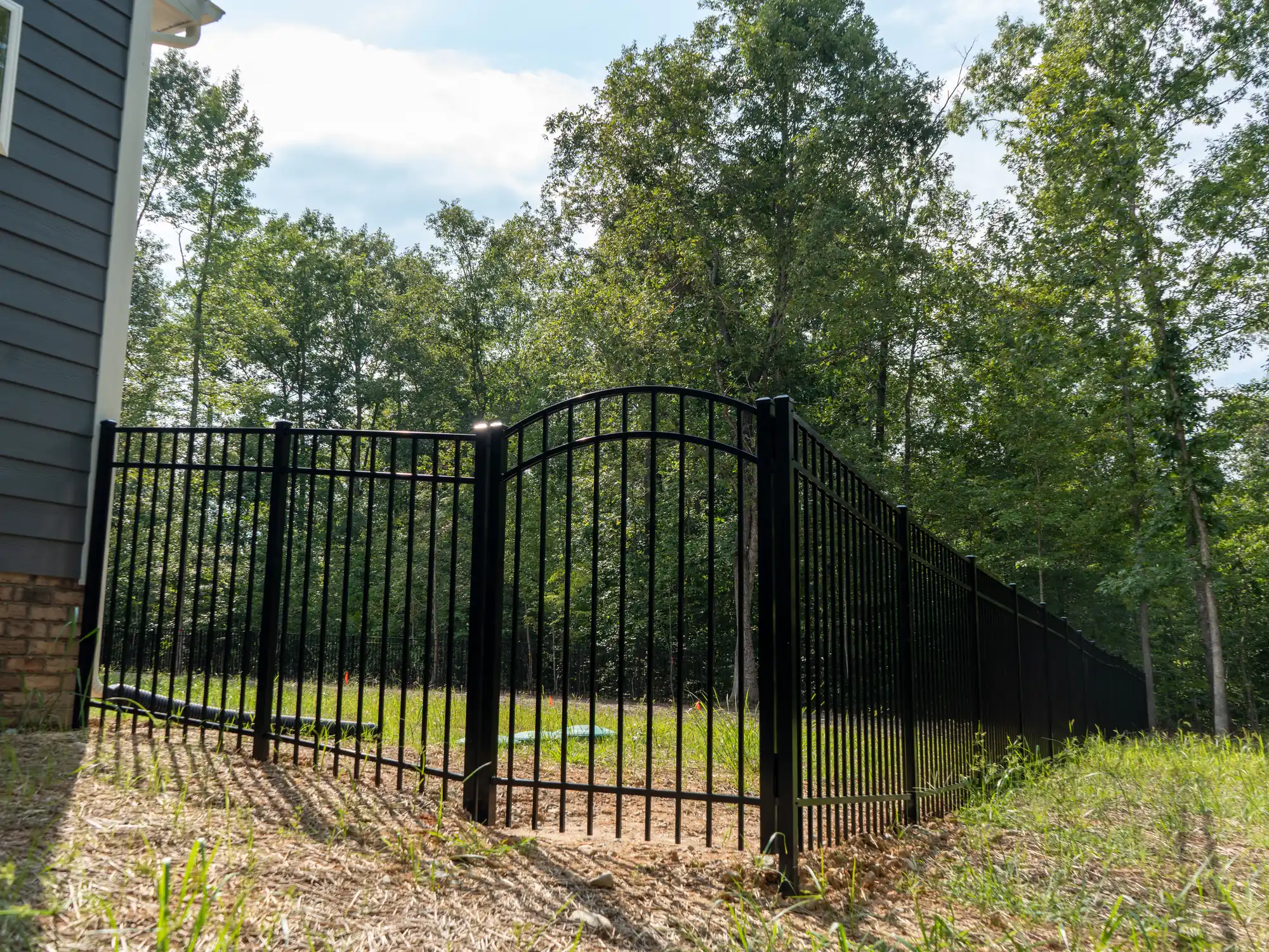 Arched black metal gate and fence line beside a new Chesterfield home