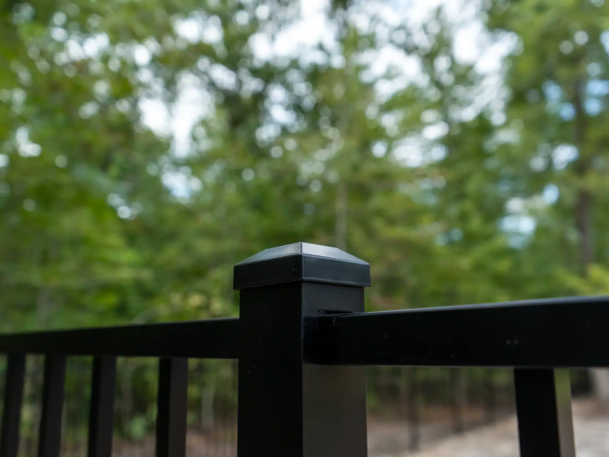 Flat cap on a black aluminum fence post with pine trees behind it