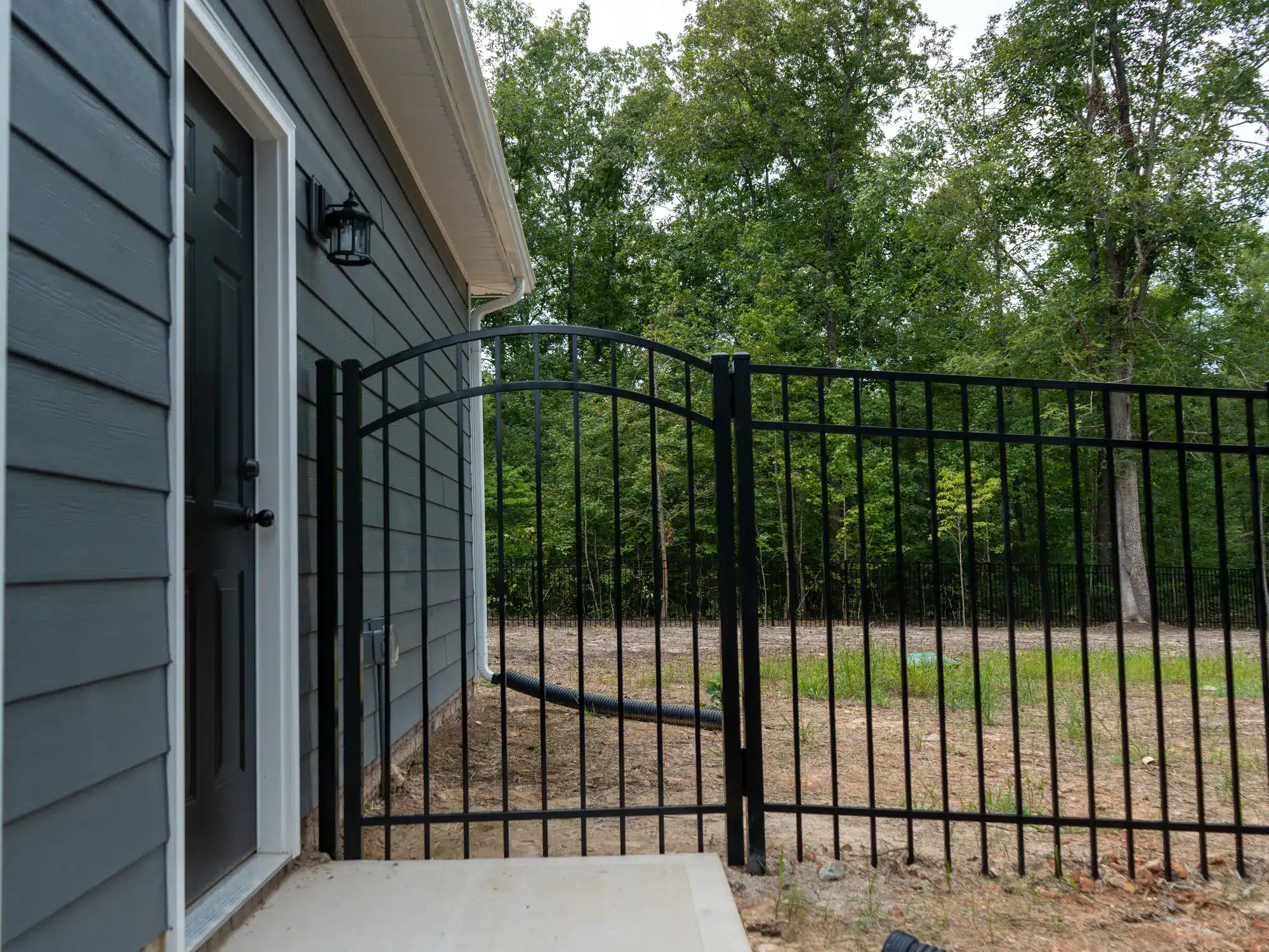 Arched black aluminum walk gate beside the side door of a gray-blue home