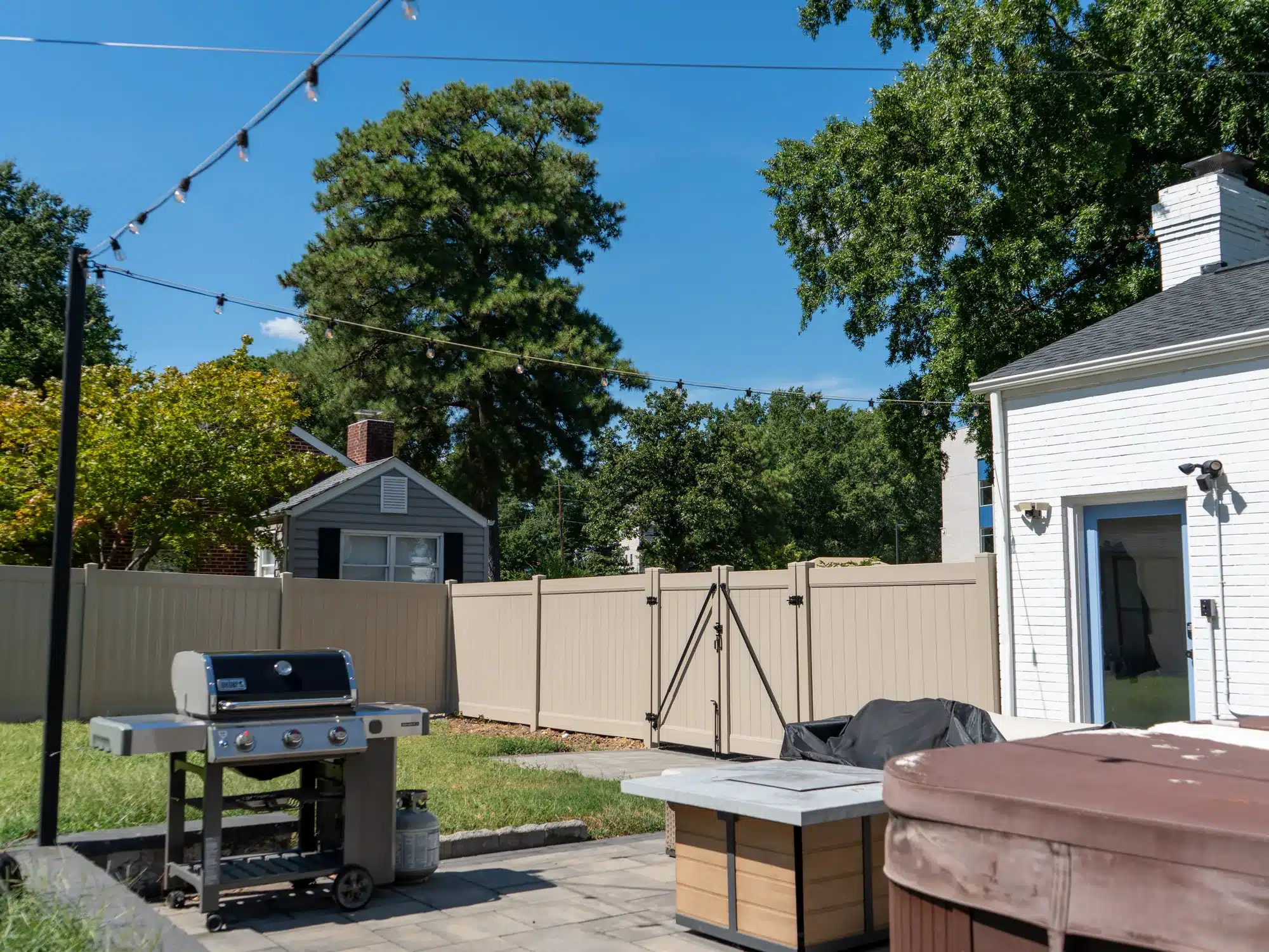 Tan backyard vinyl fence with a double gate enclosing a Henrico patio, grill and hot tub
