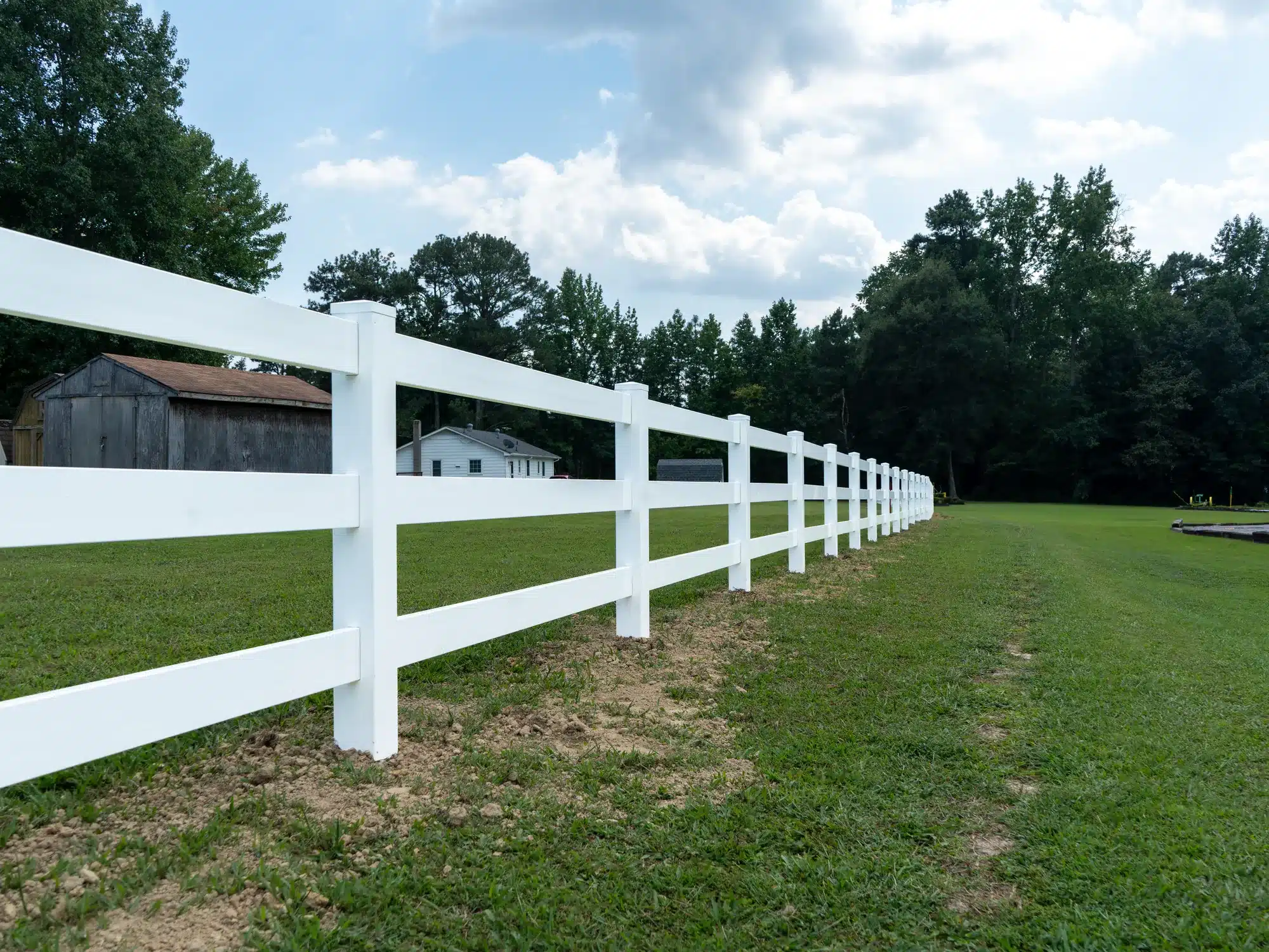 Three-rail white vinyl rail fence along a pasture with a barn in the background