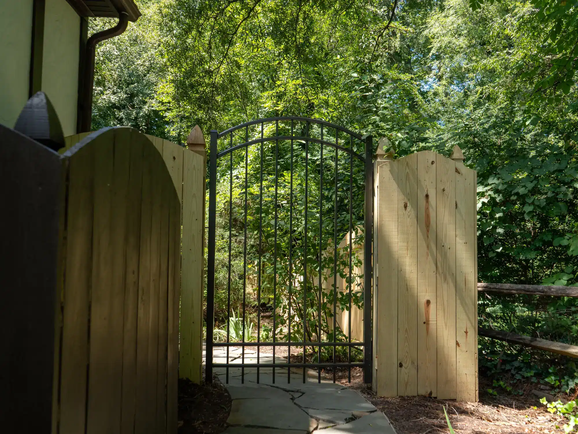 Wood privacy fence and bronze aluminum fence meeting at an arched gate in Henrico, VA
